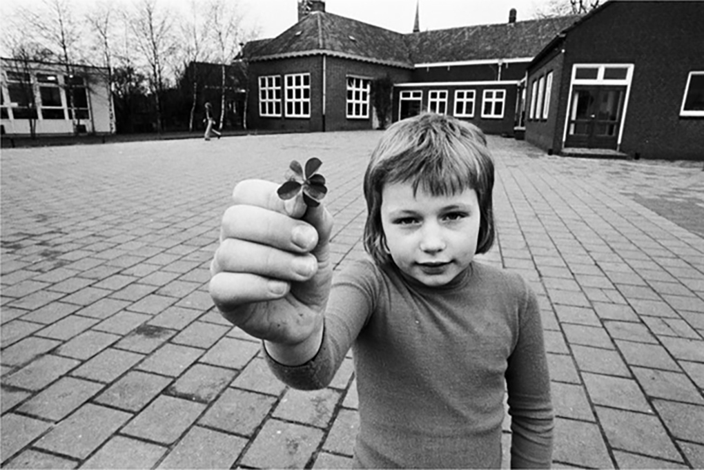 Jongen laat een klavertje vier zien, hij staat nu op de speelplaats van de Aloysius jongensschool.